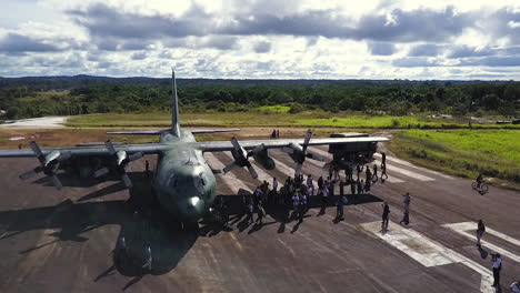 Orbital-aerial-shot-around-a-big-military-cargo-plane,-as-people-get-off-on-the-runway
