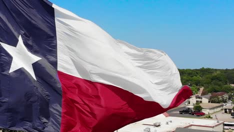 A-close-up-drone-shot-of-the-texas-flag-with-a-bright-blue-sky-and-a-glimpse-of-Wacos-city-in-the-background