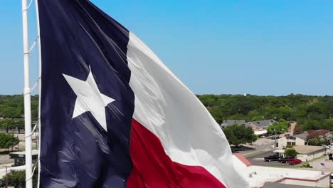A-close-up-drone-shot,panning-motion,-of-the-texas-flag-with-a-bright-blue-sky-and-a-glimpse-of-Wacos-city-in-the-background