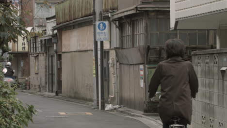 Two-different-commutes-on-the-old-street-of-Tokyo,-One-of-them-rides-a-scooter-and-another-rids-a-bike