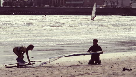 Two-people-preparing-their-windsurfing-board-on-a-beach-in-Kamakura,-Japan