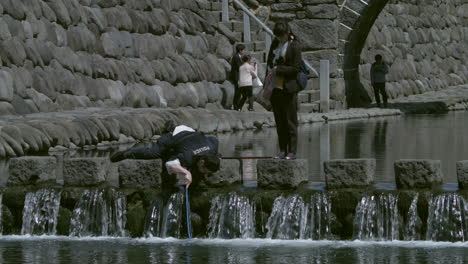 Policía-Japonés-Buscando-Algo-En-El-Agua-Con-Una-Mujer-Cuidándolo