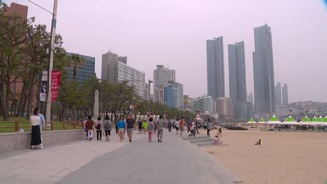 People-walking-along-the-footpath-in-Haeundae-Beach,-Busan,-South-Korea