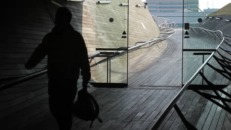 The-silhouette-of-a-man-with-a-backpack-in-his-hands-enters-through-the-automatic-glass-door-of-International-Port-Terminal-of-Yokohama,-Japan