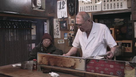 Japanese-chef-talking-to-member-of-public-at-small-Izakaya-in-Tokyo,-Japan