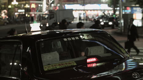 Disparo-Inclinado-Desde-Un-Taxi-Negro-Estacionado-Hasta-Grandes-Carteles-Con-Muchas-Luces-En-Tokio