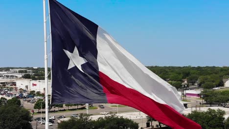 Eine-Nah-Herannahende-Drohnenaufnahme-Der-Texanischen-Flagge-Mit-Einem-Strahlend-Blauen-Himmel-Und-Einem-Blick-Auf-Die-Stadt-Wacos-Im-Hintergrund