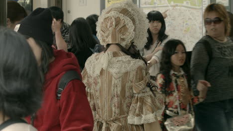Eine-Junge-Frau-In-Einem-Vintage-Kleid-Steht-Mit-Dem-Rücken-Zur-Kamera,-Während-Menschen-Im-Modernen-Tokio-Vorbeigehen