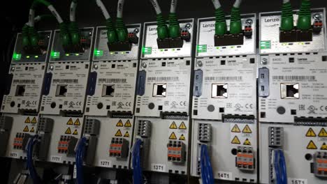 Nahaufnahme-Von-Rechts-Nach-Links-Einer-Reihe-Industrieller-Wechselrichterantriebe-Mit-Flackernden-Grünen-LEDs-In-Einem-Schaltschrank-Einer-Laufenden-Maschine