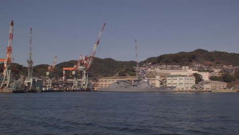 Segeln-Vorbei-An-Hafenkränen-Und-Einem-Kriegsschiff,-Das-Im-Hafen-Von-Kobe,-Japan,-Angedockt-Ist