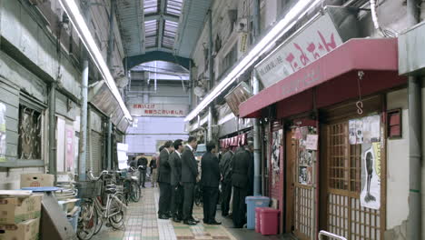 Un-Grupo-De-Personas-Bien-Vestidas-Esperando-Frente-A-Una-Tienda-En-Una-Cola-En-El-Mercado-De-La-Ciudad-Vieja-De-Tokio,-Japón