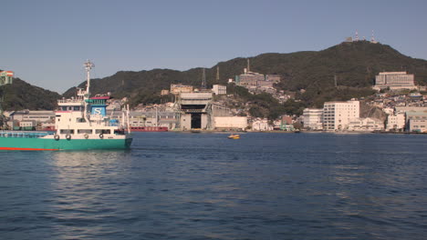 Sailing-past-boat-with-gantry-crane-in-the-background,-Kobe,-Japan