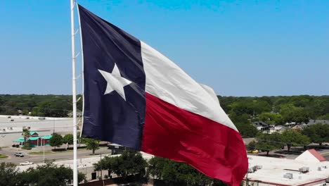 A-close-up-drone-shot-of-the-texas-flag-with-a-bright-blue-sky-and-a-glimpse-of-Wacos-city-in-the-background