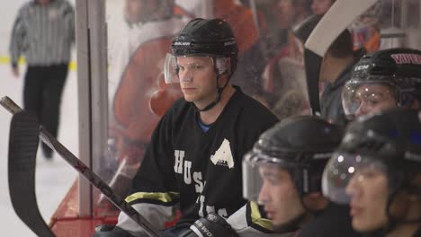 Der-Stellvertretende-Kapitän-In-Uniform-Sitzt-Auf-Der-Bank-Und-Schaut-Anderen-Eishockeyspielern-Beim-Spielen-Zu
