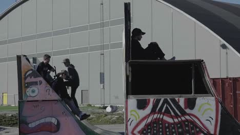 Teenagers-On-BMX-Riding-Half-Pipe-With-Giant-Hangar-In-The-Background