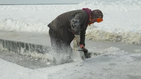 Man-cutting-blocks-of-ice-from-lake-with-chainsaw-to-build-shelter