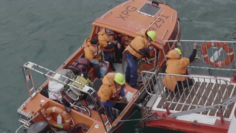 Orangefarbenes-Rettungsboot-Verlässt-Die-Bootsrampe-Sicher,-Unterstützt-Von-Einem-Besatzungsmitglied,-Das-Sich-Am-Geländer-In-Grönland-Festhält