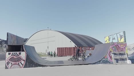 Teenage-BMX-Riding-Half-Pipe-With-Giant-Hangar-In-The-Background