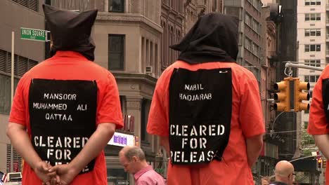 Erwachsene-Männer-Mit-Schwarzen-Kapuzen-Und-Orangefarbenen-Gefängnisoveralls-Protestieren-In-New-York