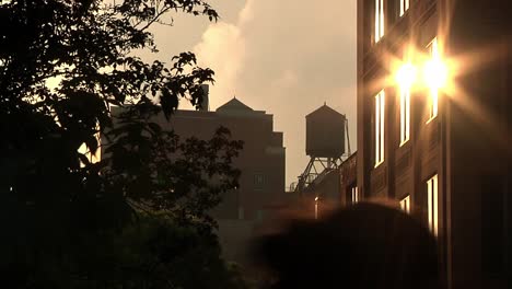 Goldgelbe-Sonnenreflexion-Auf-Einem-Mehrfamilienhaus-Mit-Wasserturm-In-Der-Ferne-In-New-York