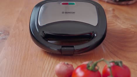 Revealing-view,-closed-electric-sandwich-grill-on-kitchen-counter-with-tomatoes