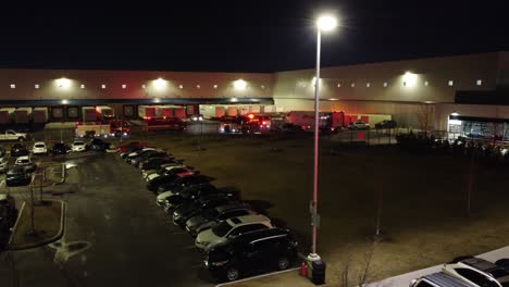 Flashing-EMS-red-blue-lights-behind-industrial-loading-dock-at-night,-aerial-parallax