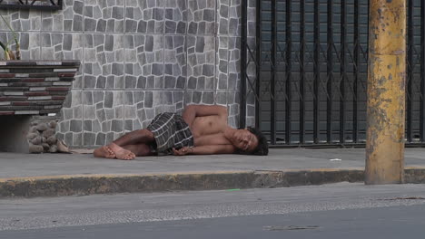 View-Of-Homeless-Adult-Topless-Male-Sleeping-On-Pavement-With-Traffic-Going-Past