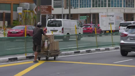 Singaporean-Man-pushing-cart-of-cardboard-boxes-in-the-middle-of-avenue---Wide-tracking-shot