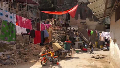 Kid-riding-his-bike-on-house-patio-near-hanging-laundry,-Zanzibar---Wide-static-shot