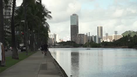 People-leisurely-walking-in-Promenade-next-to-Ala-Wai-Canal-in-Oahu,-Hawaii---Wide-Static-shot