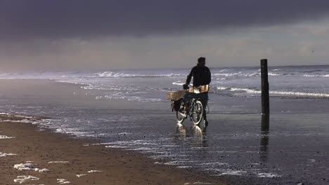 Viejo-Pescador-Caminando-Con-Su-Bicicleta-Por-La-Costa-De-La-Marisma-En-La-Playa-De-La-Isla-De-Texel,-Holanda-Del-Norte,-Países-Bajos---Amplia-Toma-Estática