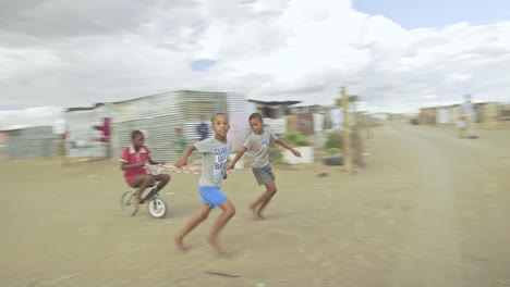 Playful-children-enjoy-riding-a-bike-fooling-around-in-Namibian-slum---Wide-panning-shot