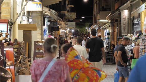 People-strolling-in-summer-along-a-street-promenade-with-stores-on-either-side-at-night