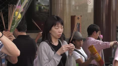 Asiatische-Frau-Mit-Geschlossenen-Augen-Hält-Räucherstäbchen-Vor-Dem-Tempel-In-Singapur