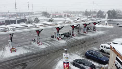 A-aerial-drone-shot-passing-through-the-forecourt-of-a-Canadian-Tire-Corporation-filling-station-during-a-snow-storm,-Mississauga,-Canada,