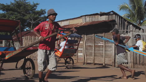 Einheimischer-Madagassischer-Mann-Zieht-Rikscha-Entlang-Der-Straße-Mit-Beifahrer-Im-Hintergrund