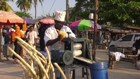 Street-Vendor-Squeezing-Fresh-Sugar-Cane-Juice-in-Unguja,-Zanzibar---Medium-shot