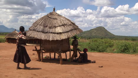 Mother-And-Child-Sitting-In-Shade-Under-Small-Thatched-Roof-Hut-In-Rwanda