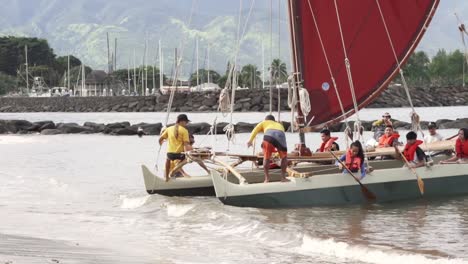 Group-of-people-entering-the-sea-and-launching-Catamaran-recreational-Polynesian-canoe---Long-medium-tracking-shot