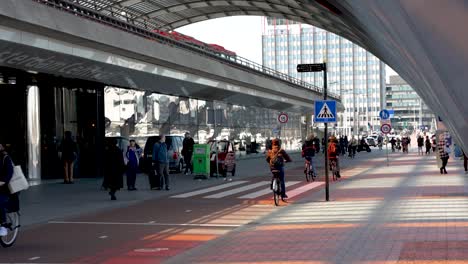 Belebter-Fahrradweg-Vor-Dem-Amsterdamer-Hauptbahnhof,-Während-Die-Menschen-Ihren-Tag-Mit-Dem-Fahrrad-In-Der-Geschäftigen-Stadt-Amsterdam,-Niederlande,-Verbringen