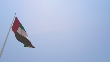 Gran-Bandera-De-Los-Eau-En-El-Poste-En-Abu-Dhabi-Ondeando-Lentamente-En-El-Viento-En-Un-Día-Soleado-Con-Cielo-Azul-Claro-Vista-De-Tierra-De-Abajo-Hacia-Arriba