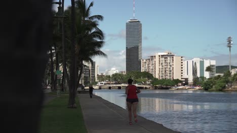 Pedestrians-exercising-in-Promenade-next-to-Ala-Wai-Canal-in-Oahu,-Hawaii---Pan-Rack-focus-shot