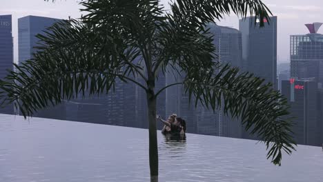 Zwei-Freunde-Posieren-Für-Fotos-Am-Infinity-Pool-In-Singapur,-Betrachtet-Durch-Einen-Baum