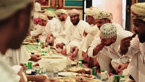 Omanische-Männer-Genießen-Gemeinsam-Ein-Traditionelles-Essen-In-Einem-Bankettsaal-Im-Nahen-Osten-–-Mittlere-Diaaufnahme