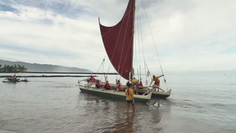 People-launching-into-sea-a-Polynesian-double-hulled-voyaging-canoe---Static-wide-shot