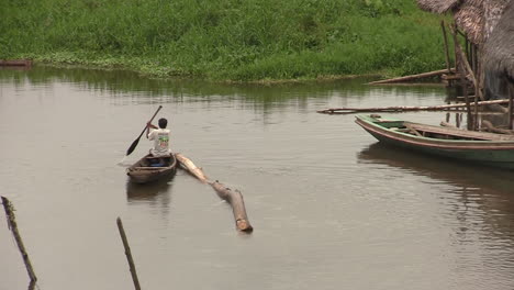 Adult-Male-Padding-On-Boat-With-Tree-Log-Tied-To-It-On-River