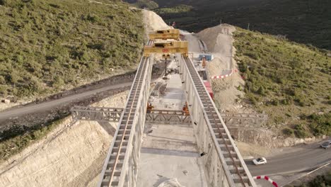 Vídeo-De-Vuelo-Hacia-Atrás-Sobre-La-Estructura-De-Un-Nuevo-Puente-En-Construcción-En-El-Barranco-De-La-Bota-En-Morella,-Que-Muestra-Grúas-Y-Vías-De-Ferrocarril-Desde-Arriba.