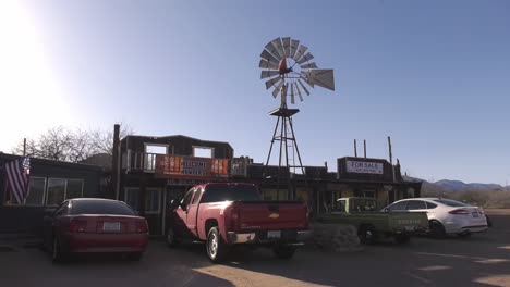 Geparkte-Fahrzeuge-Vor-Einem-Gemischtwarenladen-Mit-Langsam-Rotierender-Windmühle-In-Arizona