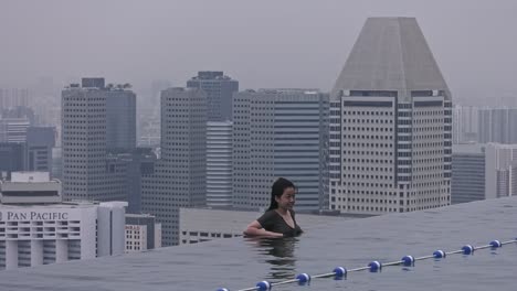 Hermosa-Chica-Apoyada-En-El-Borde-De-La-Piscina-Infinita-De-Marina-Bay-Sands-En-Singapur---Plano-Estático-Amplio