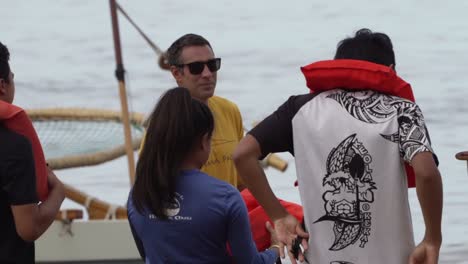 Teenager-tourists-putting-on-life-jackets,-preparing-for-sailing-on-a-Catamaran-in-Oahu,-Hawaii---Pan-left-close-up-shot